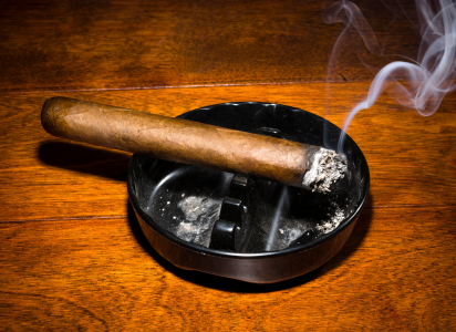 burning cigarette resting in cheap ashtray